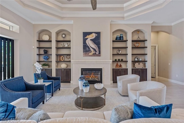 living area with ornamental molding, built in features, a tray ceiling, and light wood finished floors