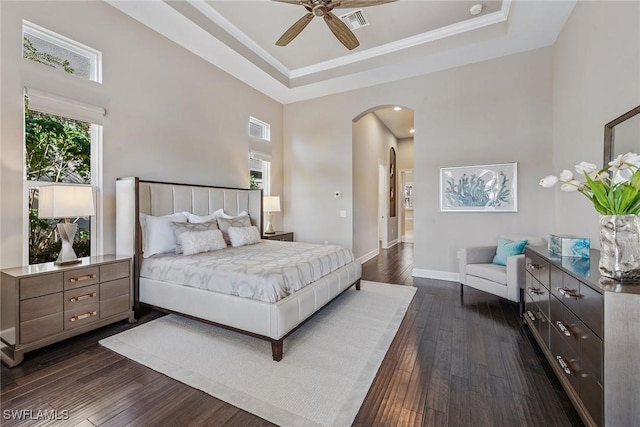 bedroom with a tray ceiling, baseboards, visible vents, arched walkways, and dark wood-type flooring