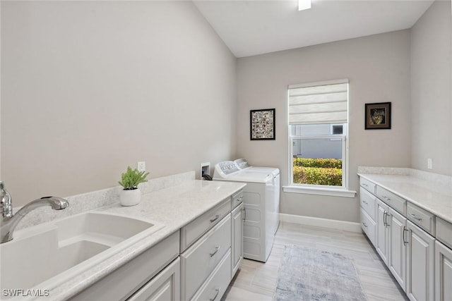 washroom with baseboards, cabinet space, washing machine and dryer, and a sink