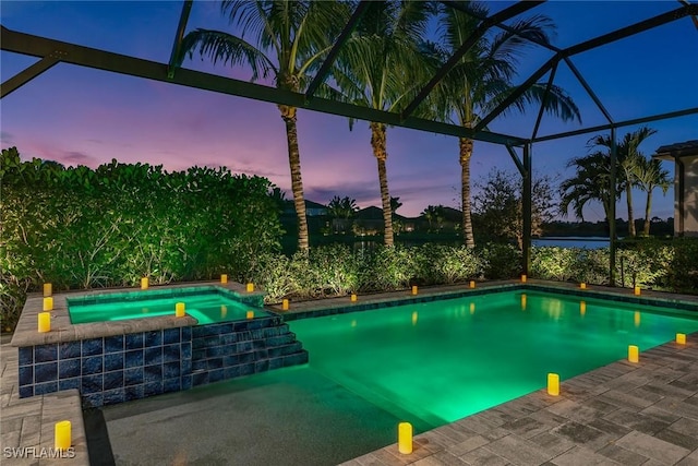 pool at dusk featuring a pool with connected hot tub, a lanai, and a patio area