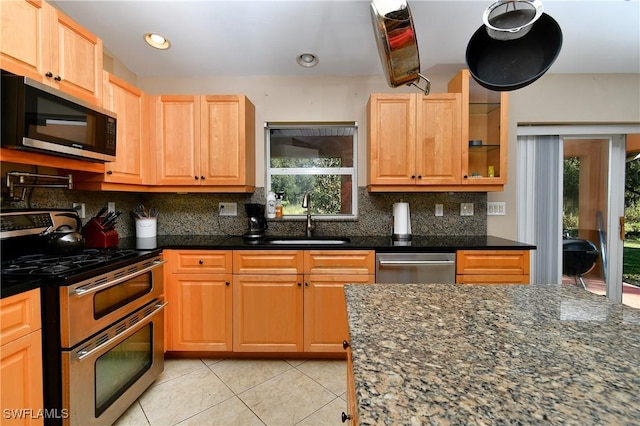 kitchen with light tile patterned floors, stainless steel appliances, decorative backsplash, a sink, and dark stone countertops