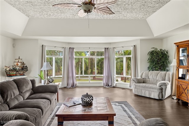 living room featuring dark wood-type flooring, ceiling fan, a healthy amount of sunlight, and a raised ceiling