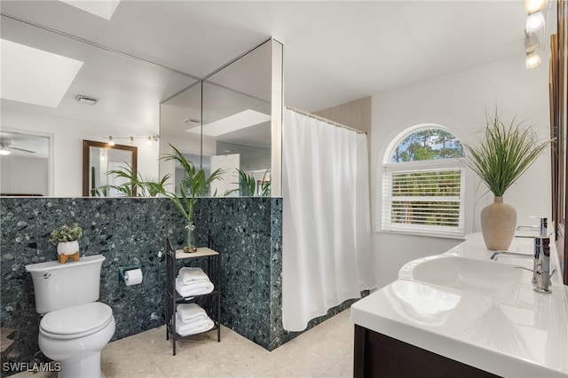 bathroom with a skylight, toilet, ceiling fan, vanity, and tile patterned flooring