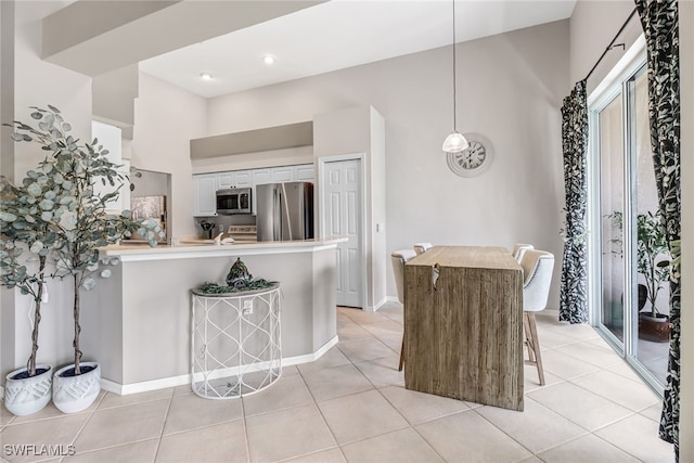 kitchen with a breakfast bar area, hanging light fixtures, stainless steel appliances, light tile patterned flooring, and white cabinetry