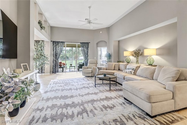 living area with arched walkways, a ceiling fan, tile patterned flooring, and a towering ceiling