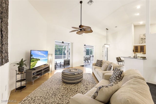 living room with a towering ceiling, light hardwood / wood-style floors, and ceiling fan