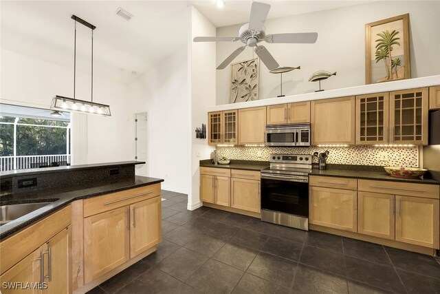 kitchen featuring a high ceiling, hanging light fixtures, light brown cabinetry, appliances with stainless steel finishes, and tasteful backsplash