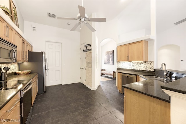 kitchen with dark tile patterned floors, kitchen peninsula, tasteful backsplash, appliances with stainless steel finishes, and ceiling fan