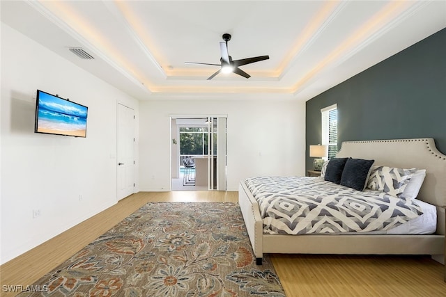 bedroom featuring light hardwood / wood-style floors, access to outside, a raised ceiling, and ceiling fan