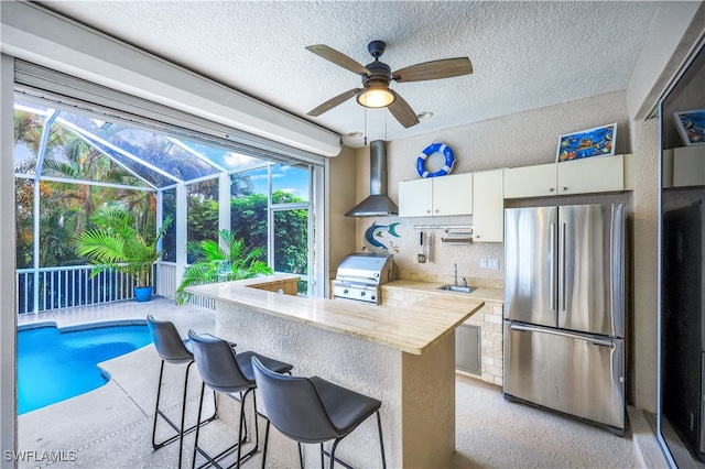 kitchen with kitchen peninsula, white cabinetry, a kitchen bar, and stainless steel refrigerator