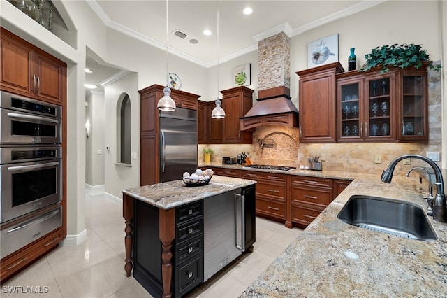 kitchen featuring custom range hood, stainless steel appliances, sink, decorative light fixtures, and light stone counters