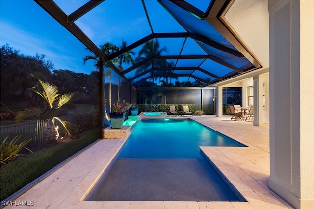 pool at dusk with an in ground hot tub, a patio area, and glass enclosure