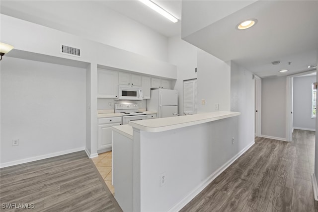 kitchen with kitchen peninsula, white cabinets, a breakfast bar, light wood-type flooring, and white appliances