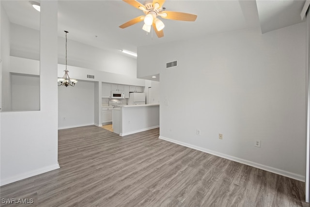 unfurnished living room with high vaulted ceiling, ceiling fan with notable chandelier, and hardwood / wood-style floors