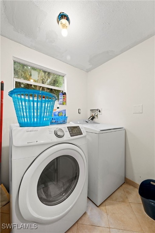 clothes washing area featuring a textured ceiling, light tile patterned flooring, and washer and clothes dryer