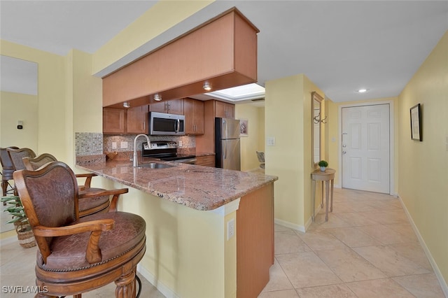 kitchen with tasteful backsplash, light stone countertops, sink, kitchen peninsula, and stainless steel appliances