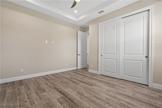 unfurnished bedroom featuring light hardwood / wood-style floors, a closet, a tray ceiling, and ceiling fan