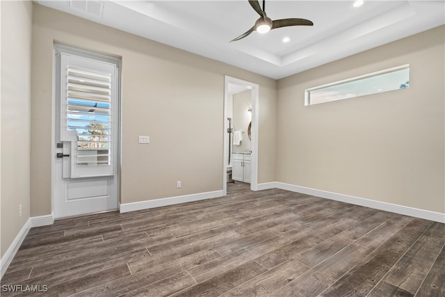 empty room featuring ceiling fan, plenty of natural light, dark wood-type flooring, and a tray ceiling