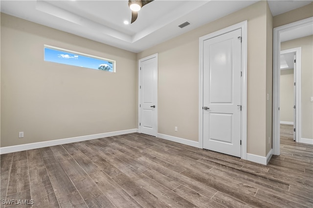 unfurnished bedroom featuring ceiling fan, hardwood / wood-style flooring, and a tray ceiling