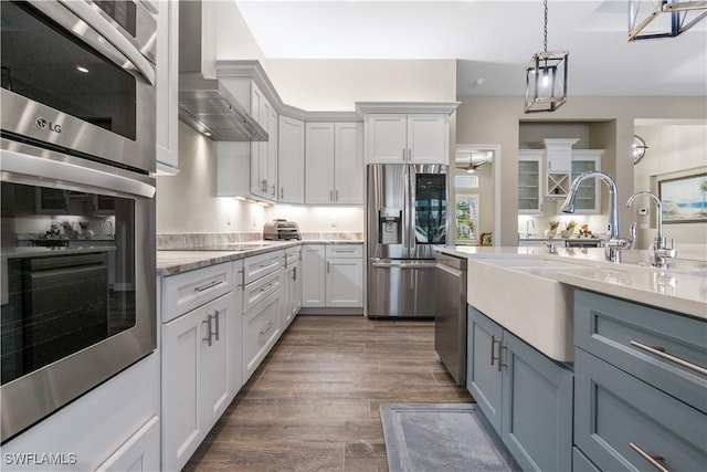 kitchen with hanging light fixtures, dark hardwood / wood-style flooring, wall chimney exhaust hood, appliances with stainless steel finishes, and white cabinets