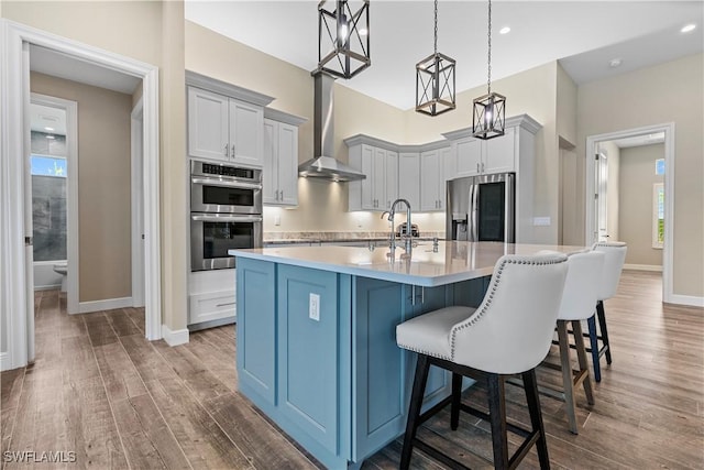 kitchen featuring appliances with stainless steel finishes, decorative light fixtures, light hardwood / wood-style flooring, a center island with sink, and a breakfast bar area