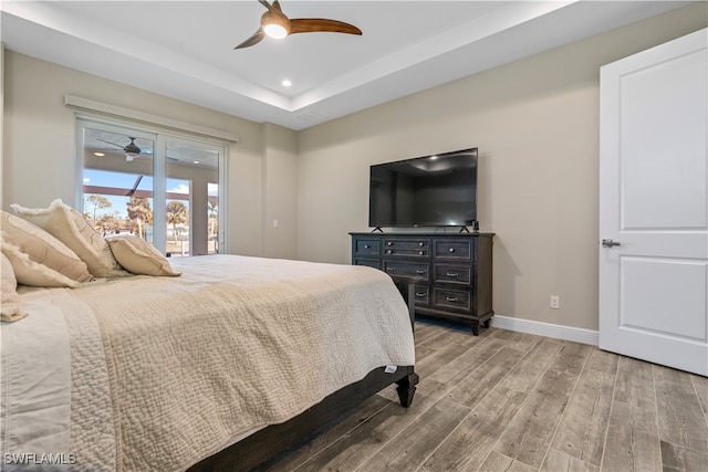 bedroom featuring ceiling fan, a raised ceiling, access to outside, and wood-type flooring