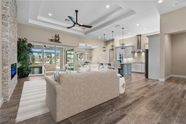 living room with ceiling fan, a tray ceiling, and a fireplace