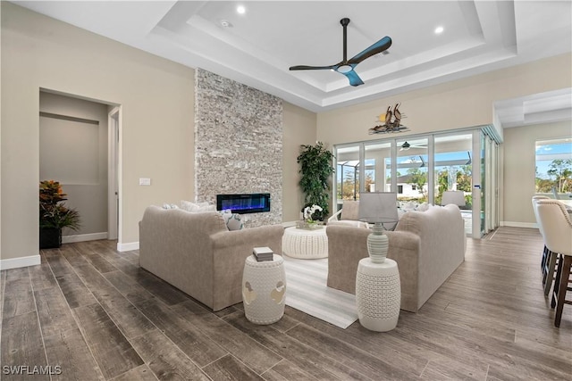 living room featuring ceiling fan, a stone fireplace, and a raised ceiling