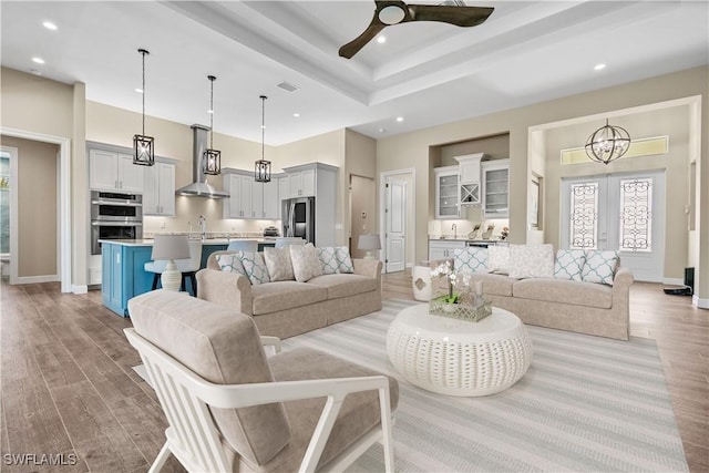 living room with light wood-type flooring, ceiling fan with notable chandelier, french doors, and sink