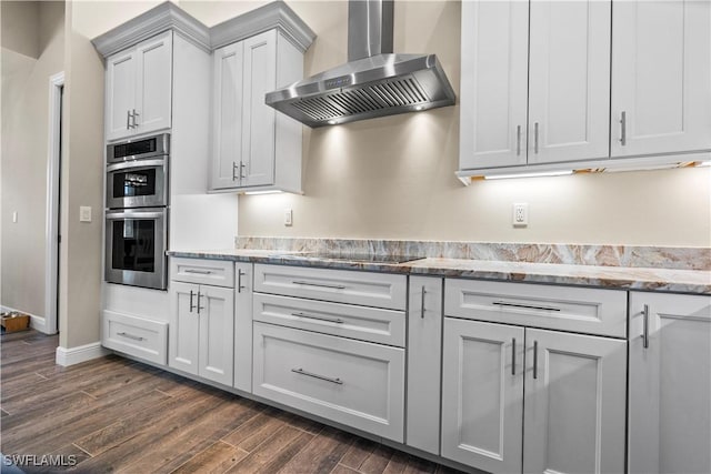 kitchen featuring stainless steel double oven, dark wood-type flooring, wall chimney range hood, stone countertops, and black electric cooktop