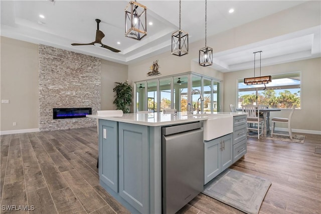 kitchen with an island with sink, a raised ceiling, pendant lighting, and dark hardwood / wood-style flooring