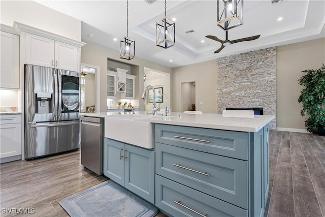 kitchen with appliances with stainless steel finishes, hanging light fixtures, white cabinets, sink, and a tray ceiling