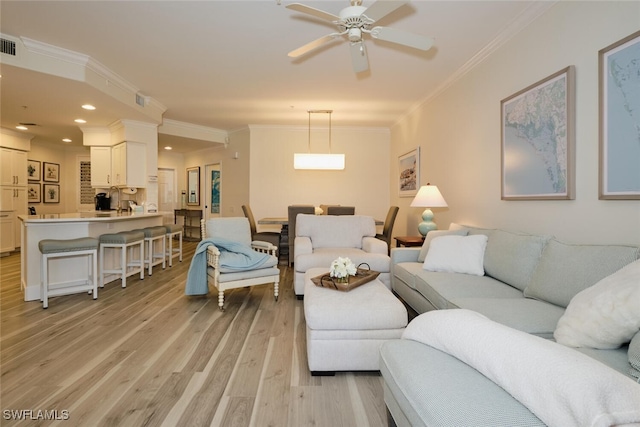 living room with ornamental molding, light wood-type flooring, and ceiling fan