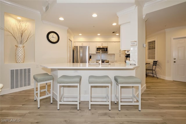 kitchen featuring kitchen peninsula, white cabinets, a kitchen bar, light hardwood / wood-style floors, and stainless steel appliances