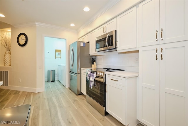 kitchen featuring washing machine and dryer, appliances with stainless steel finishes, white cabinets, ornamental molding, and light hardwood / wood-style flooring