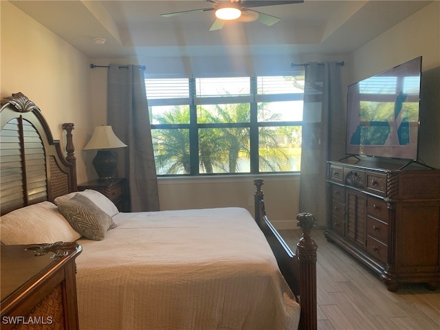 bedroom featuring light wood-type flooring, a tray ceiling, and ceiling fan