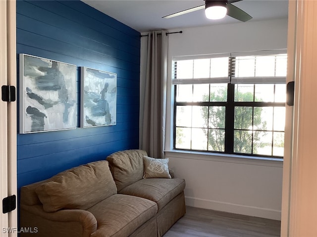 sitting room featuring wood walls, hardwood / wood-style flooring, ceiling fan, and plenty of natural light