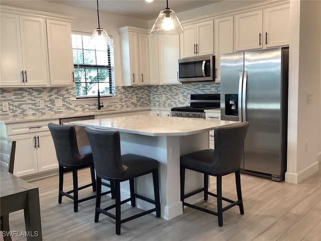 kitchen featuring tasteful backsplash, white cabinetry, appliances with stainless steel finishes, decorative light fixtures, and light wood-type flooring