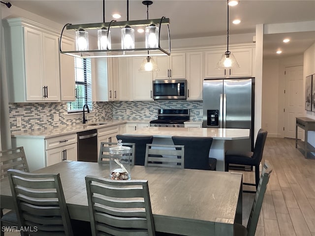 kitchen featuring white cabinetry, sink, appliances with stainless steel finishes, decorative light fixtures, and light wood-type flooring