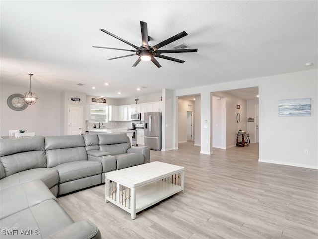 living room with a textured ceiling, light hardwood / wood-style floors, and ceiling fan with notable chandelier