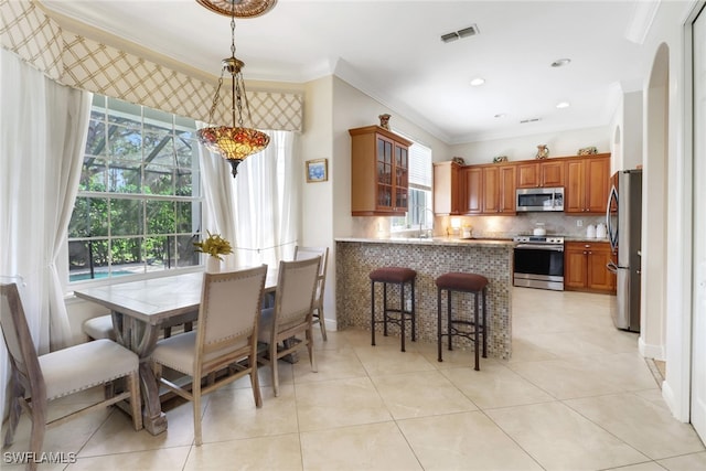 kitchen with tasteful backsplash, appliances with stainless steel finishes, kitchen peninsula, decorative light fixtures, and crown molding