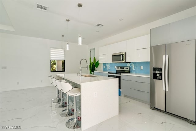 kitchen with hanging light fixtures, stainless steel appliances, backsplash, a center island with sink, and sink