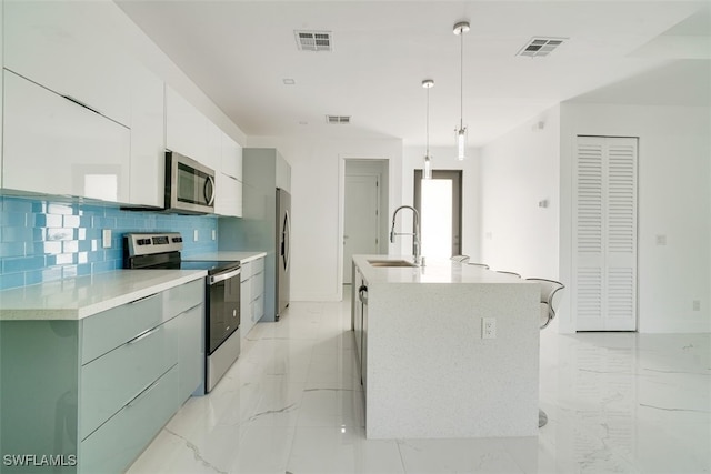 kitchen featuring tasteful backsplash, an island with sink, appliances with stainless steel finishes, sink, and decorative light fixtures