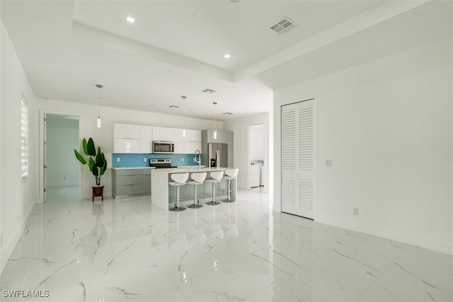 kitchen with backsplash, an island with sink, white cabinetry, stainless steel appliances, and decorative light fixtures