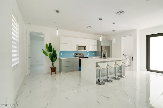 kitchen with appliances with stainless steel finishes, backsplash, pendant lighting, and a large island with sink