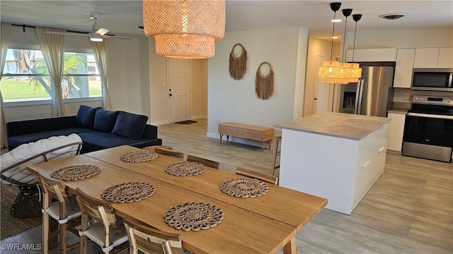 dining room with ceiling fan with notable chandelier and light wood-type flooring