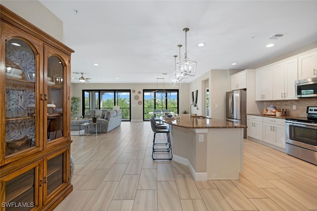 kitchen featuring appliances with stainless steel finishes, hanging light fixtures, white cabinets, a center island with sink, and dark stone counters