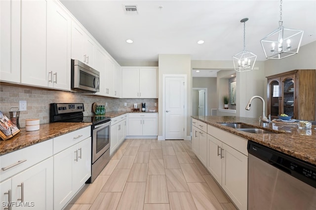 kitchen with sink, white cabinetry, hanging light fixtures, appliances with stainless steel finishes, and dark stone counters