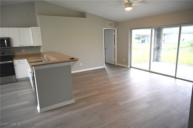 kitchen featuring kitchen peninsula, lofted ceiling, appliances with stainless steel finishes, white cabinetry, and light hardwood / wood-style flooring