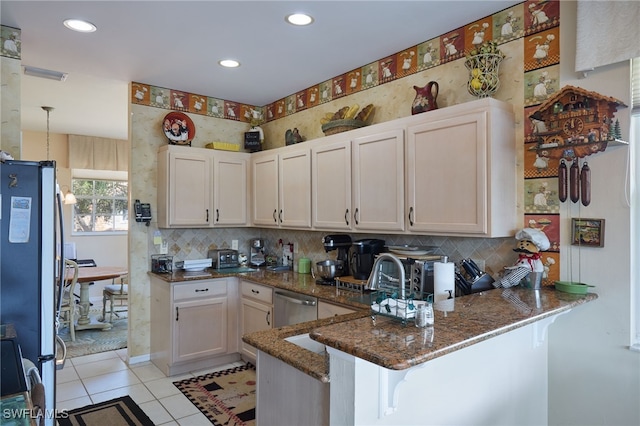 kitchen with dark stone countertops, appliances with stainless steel finishes, light tile patterned floors, and kitchen peninsula